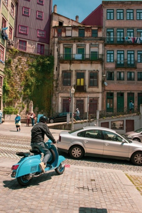 Creative architecture of homes in Porto, Portugal- photographed by Tiago with the Shots. The homes are built on a hill, photographed in the photo is a man on a motorcycle and numerous cars adn people.